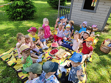 Zdjęcie przedstawia całą grupę dzieci, które siedzą na kocyku podczas pikniku.