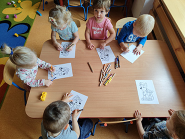 Zdjęcie przedstawia sześcioro dzieci, które siedzą przy stoliku i kolorują obrazek.