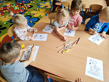 Zdjęcie przedstawia pięcioro dzieci, które siedzą przy stoliku i kolorują obrazek.