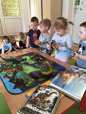 Na zdjęciu widać czworo dzieci przy stoliku oglądające sylwetki dinozaurów.
