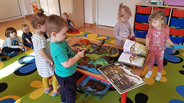 Na zdjęciu widać grupę dzieci oglądające książki i dinozaury.