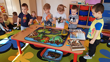 Na zdjęciu widać chłopców i dziewczynki przy stoliku z dinozaurami