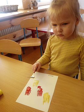 Dziewczynka odbija widelec umoczony w farbie na kartce papieru.