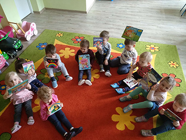 dzieci siedzą na dywanie i trzymają kolorowe książeczki
