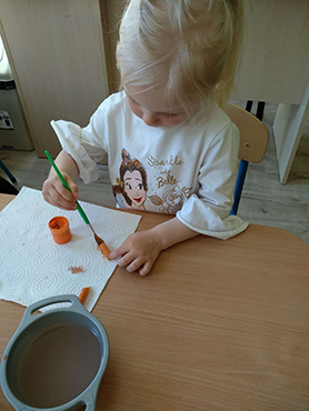 Dziewczynka maluje pomarańczową farbą makaron