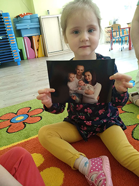 Dziewczynka prezentuje zdjęcie swojej rodziny, które przyniosła do żłobka