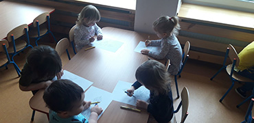 Na zdjęciu widać dzieci siedzące przy stolikach, które kolorują swoje obrazki.