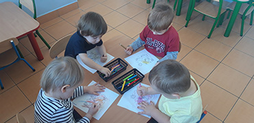 Dzieci siedzące przy stolikach,  kolorują kredkami 