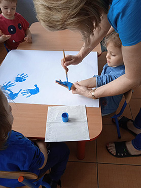 Pani maluje dziewczynce rączkę niebieska farbą.
