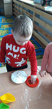 Chłopiec  wysiewający nasionka rzeżuchy na spodek z watą.