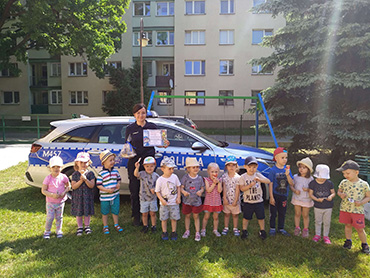 Dzieci razem z panią policjantką stoją przy radiowozie policyjnym