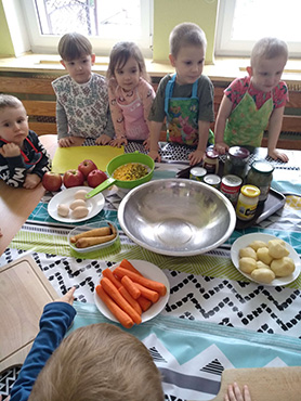 Dzieci stoją przy stoliku, na którym są przygotowane warzywa do naszej Tygrysiej sałatki jarzynowej