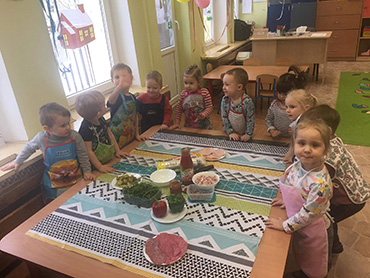 na zdjęciu widać dzieci stojące przy stoliku, na którym są przygotowane produkty do naszej tygrysiej pizzy
