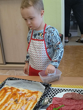 chłopczyk posypuje pokrojoną szynką spód pizzy
